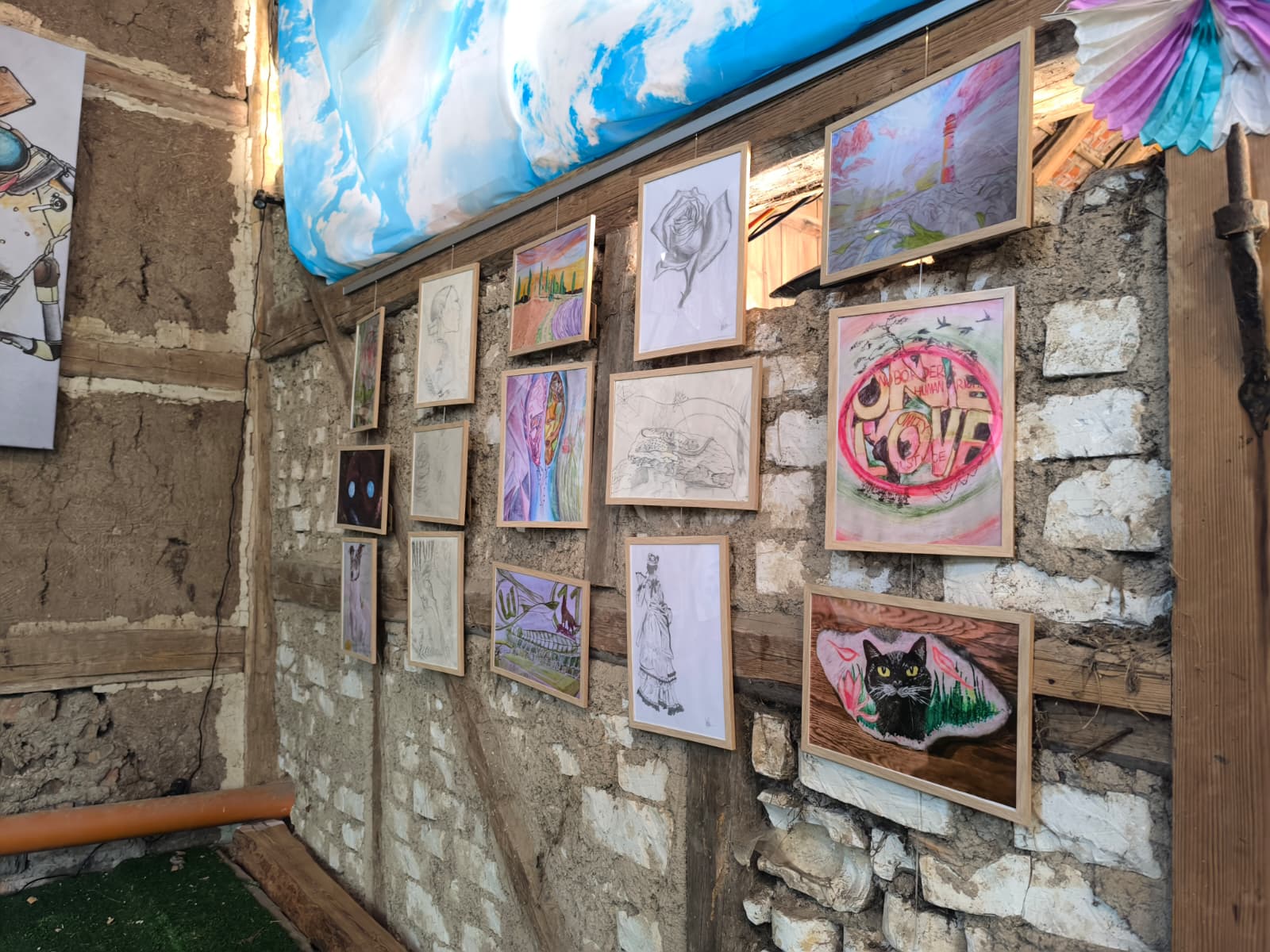 Interior view of the creative barn studio with artwork displayed on rustic stone walls, including watercolors, sketches, and nature-inspired art pieces arranged in a gallery-style presentation